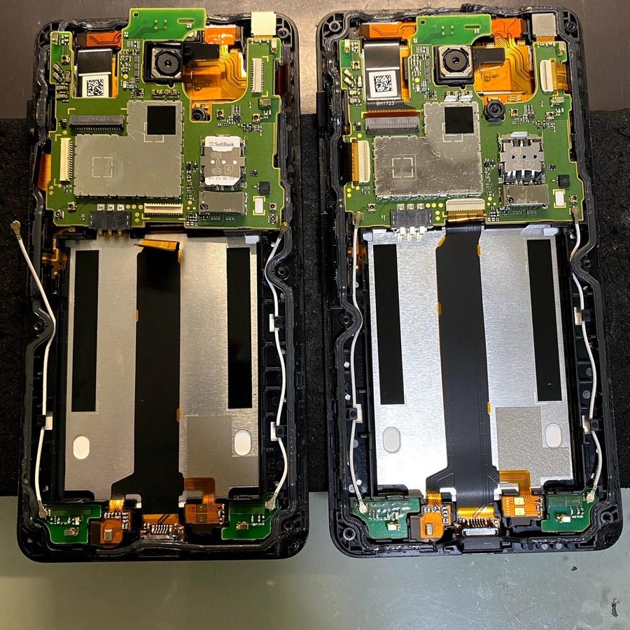 分解したスマートフォン2台の基板とフレームを並べて部品を確認している写真